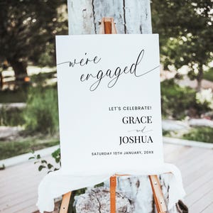 May include: White sign with black text announcing an engagement party for Grace and Joshua. The sign reads "We're engaged! Let's celebrate! Grace and Joshua. Saturday 10th January, 20XX."