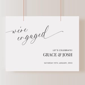 May include: White sign with black calligraphy that reads "we're engaged" and "Let's Celebrate! Grace & Josh Saturday 10th January, 20XX"