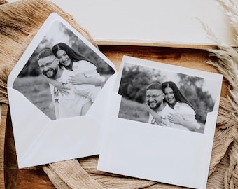 Può includere: Due fotografie in bianco e nero di una coppia che sorride e si abbraccia. Le foto sono posizionate su una superficie di legno con un tessuto beige sottostante.