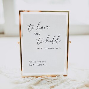 May include: A gold-framed sign with the text "to have and to hold, in case you get cold!" and "Please take one, Ava + Lucas".
