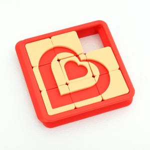 May include: A red and cream-coloured heart-shaped puzzle. The puzzle is composed of several interlocking pieces within a square frame. The heart design is visible in the centre of the puzzle.