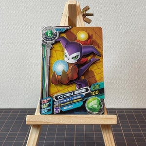 May include: A collectible trading card featuring a purple Impmon character with a white face, green eyes, and a red scarf. The card has Japanese text and various stats, including a level 6 indicator and a power rating of 600.