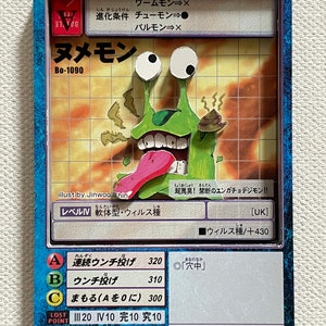 Op de afbeelding: Digimon-verzamelkaart met een groen stripfiguur met grote ogen, een lange roze tong en een bruine hoop afval. De kaart heeft Japanse tekst en een blauwe rand. De kaart is rechthoekig.
