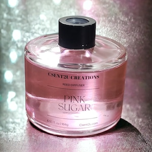 May include: A clear glass reed diffuser with a black cap, filled with pink liquid. The label reads "PINK SUGAR" and "CSENT2U CREATIONS". The bottle contains 6.50 fl oz (184g).