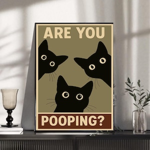 Könnte beinhalten: Ein rechteckiges Wandposter mit drei schwarzen Katzensilhouetten mit großen Augen, die von oben und unten auf einem olivfarbenen Hintergrund hervorschauen. Der Text ARE YOU ist oben und POOPING? unten in beigefarbener Schrift gedruckt.