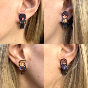 May include: Four pixelated character earrings are displayed, each with a unique design. The earrings feature a variety of colors, including black, blue, brown, and yellow. The earrings are worn on ears.