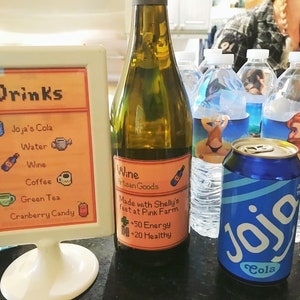 Pu&ograve; includere: Un cartello con la parola "Drinks" in lettere pixelate, che elenca Joja's Cola, Water, Wine, Coffee, Green Tea e Cranberry Candy. Una bottiglia di vino con un'etichetta che recita "Wine Artisan Goods Made with Shelly's feet at Pink Farm +50 Energy +20 Healthy". Una lattina di Joja Cola.