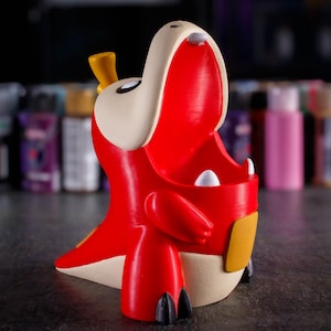 May include: Red and white 3D printed figurine of a cartoon dinosaur with its mouth open. The dinosaur has a yellow horn on its head and a yellow patch on its side.