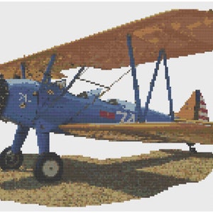 May include: A blue and brown biplane with a red, white, and blue tail. The plane is sitting on a sandy surface.