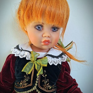 May include: A porcelain doll with red hair, wearing a burgundy dress with a black velvet vest and a green ribbon. The doll has blue eyes and a white lace collar.