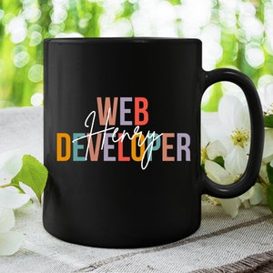 May include: Black coffee mug with the text "WEB DEVELOPER" in colorful letters and the name "Henry" written in cursive.