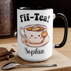 May include: White ceramic mug with a black rim and handle. The mug has a cartoon illustration of a teacup with a smiling face and the text "Fif-Tea!" and "Sophia".