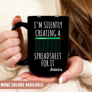 May include: Black coffee mug with white text that reads "I'm silently creating a spreadsheet for it" with a green spreadsheet icon and the name "Jessica" at the bottom.