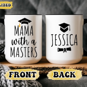 May include: Two white ceramic mugs with black handles and rims. One mug says "MAMA with a MASTERS" with a graduation cap graphic. The other mug says "JESSICA" with a diploma graphic and graduation cap. The mugs are on a wooden surface.
