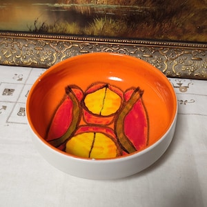 May include: A white ceramic bowl with an orange rim and a colourful abstract design in shades of red, yellow, and green.