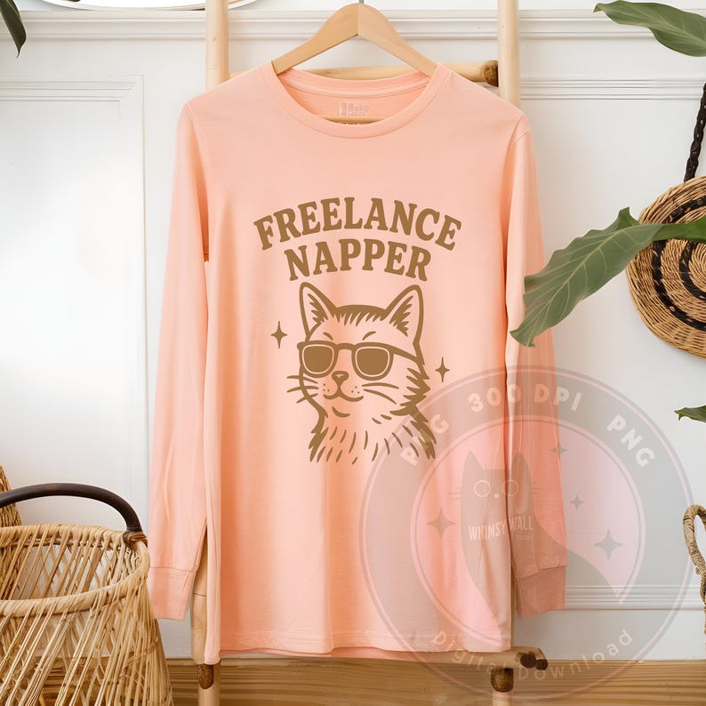 This illustration shows a shaggy cartoon cat in sunglasses, radiating lazy day energy. “Freelance Napper” is written above the head in thick, arched font. Stars add sparkle to the scene. The artwork is delivered as a high-resolution PNG with a transparent background. Great for sublimation, stickers, or introvert humor. This is a digital item only—no shipping involved.