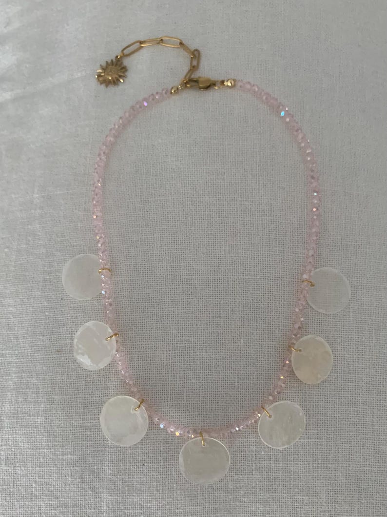 Pode incluir: Um colar delicado com uma corrente de pequenas contas rosa claro. O colar &eacute; adornado com seis pingentes redondos de concha branca e uma corrente dourada com um pingente de sol.