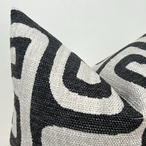 May include: Black and white patterned throw pillow with a geometric design. The pillow is made of a textured fabric.