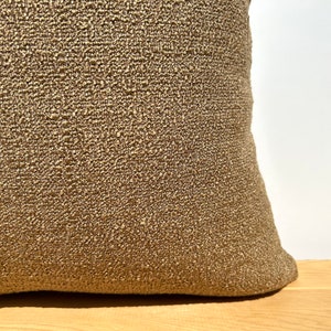 May include: A close-up of a brown throw pillow with a textured fabric. The pillow is sitting on a wooden surface.