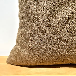 May include: A close-up of a brown throw pillow with a textured fabric. The pillow is made of a woven material with a subtle sheen.