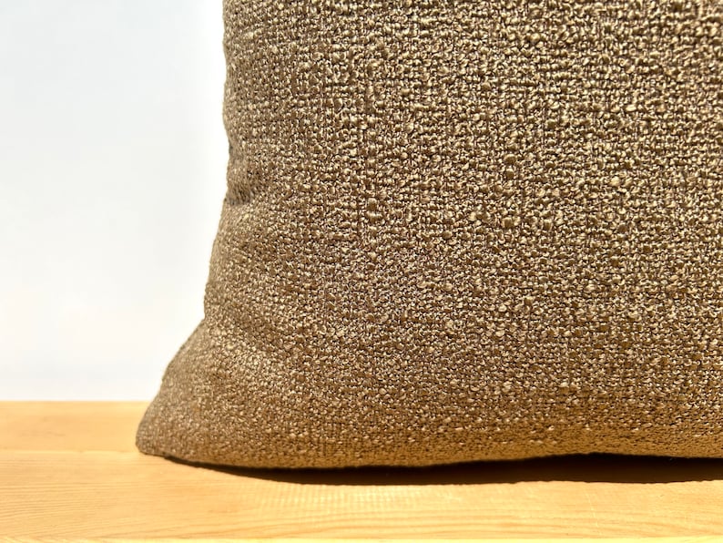 May include: A close-up of a brown throw pillow with a textured fabric. The pillow is made of a woven material with a subtle sheen.