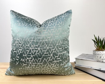 May include: A teal blue throw pillow with a white geometric pattern. The pillow is made of a soft, luxurious fabric and has a subtle sheen.