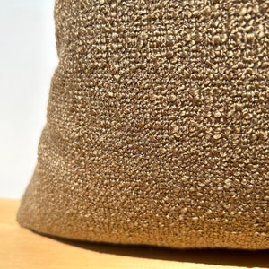 May include: Close-up of a brown textured fabric pillow. The fabric has a woven, almost bumpy texture.