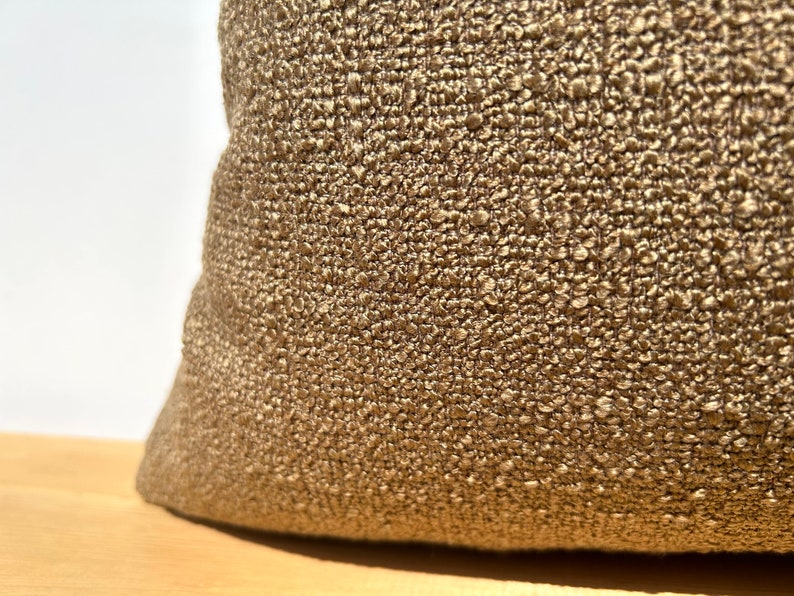 May include: Close-up of a brown textured fabric pillow. The fabric has a woven, almost bumpy texture.