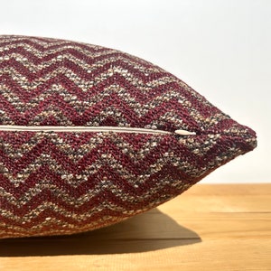 Puede incluir: Una almohada de tiro con estampado de chevron burdeos y dorado con cierre de cremallera.