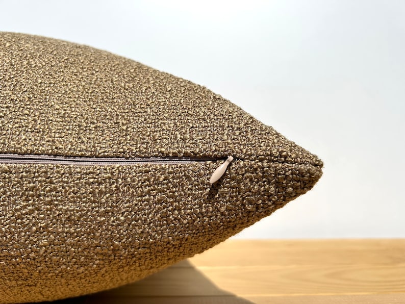 May include: Close-up of a brown throw pillow with a zipper closure. The pillow is made of a textured fabric.
