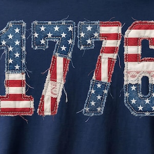 Peut inclure: T-shirt bleu marine avec le chiffre "1776" dans un design patriotique. Les chiffres sont faits de tissu denim avec des rayures rouges et blanches et des étoiles bleues, évoquant le drapeau américain. Un vêtement festif et célébratif.
