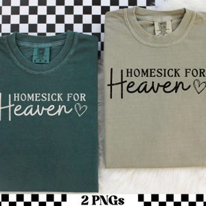 May include: Two Comfort Colors t-shirts, one teal and one khaki, are displayed. Each shirt has the phrase "Homesick for Heaven" printed on the front, with a heart symbol. The shirts are folded and presented on a checkered background.