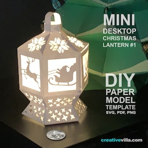 May include: A white paper lantern with a Christmas theme. The lantern is lit from inside and features a reindeer, Santa Claus in a sleigh, and snowflakes. The lantern is a DIY paper model template that can be downloaded in SVG, PDF, and PNG formats. The text "MINI DESKTOP CHRISTMAS LANTERN #1" and "DIY PAPER MODEL TEMPLATE SVG, PDF, PNG" is visible on the image.
