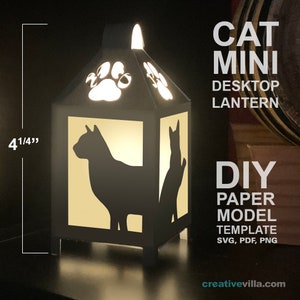 Könnte beinhalten: Eine schwarze Papiermodell-Katzenlaterne mit einem Pfotenabdruck-Design auf der Oberseite. Die Laterne ist beleuchtet und 4 1/4 Zoll hoch. Der Text "CAT MINI DESKTOP LANTERN DIY PAPER MODEL TEMPLATE SVG, PDF, PNG creativevilla.com" ist im Bild sichtbar.