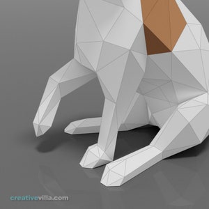 Pu&ograve; includere: Un cane di origami bianco con macchie marroni &egrave; seduto su una superficie grigia. Il cane &egrave; fatto di carta e ha un design geometrico.