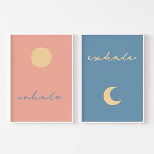 May include: Two framed prints with a minimalist design. The left print has a peach background with a yellow sun and the text "inhale" in blue. The right print has a blue background with a yellow crescent moon and the text "exhale" in yellow.