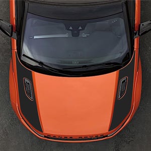 Può includere: Una vista dall'alto di un veicolo Range Rover arancione con strisce nere sul cofano, specchietti laterali neri e prese d'aria nere. Il parabrezza anteriore è visibile con tergicristalli neri e una barra interna argentata sul cruscotto.