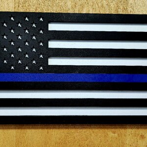 May include: A wooden American flag with a blue stripe across the middle, representing the thin blue line. The flag is painted black and white with a blue stripe.