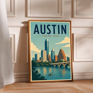 May include: A framed art print featuring a stylized illustration of the Austin, Texas skyline. The image displays tall buildings, a bridge over a river, and a person in a kayak. The text AUSTIN TEXAS, USA is printed in dark blue and orange.