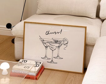 May include: A framed print with a white background and black line drawing of three martini glasses with olives and a lemon twist. The print has a wooden frame and the text "Cheers!" is written in black cursive lettering.