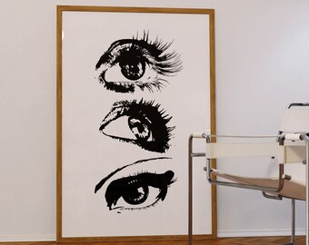 Puede incluir: Una impresión en blanco y negro enmarcada de tres ojos estilizados con pestañas. La impresión está sobre un fondo blanco y está enmarcada en un marco de madera claro.