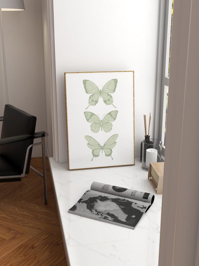 May include: A framed print featuring three green butterflies on a white background. The butterflies are arranged vertically, with the largest butterfly at the top and the smallest butterfly at the bottom. The frame is gold.