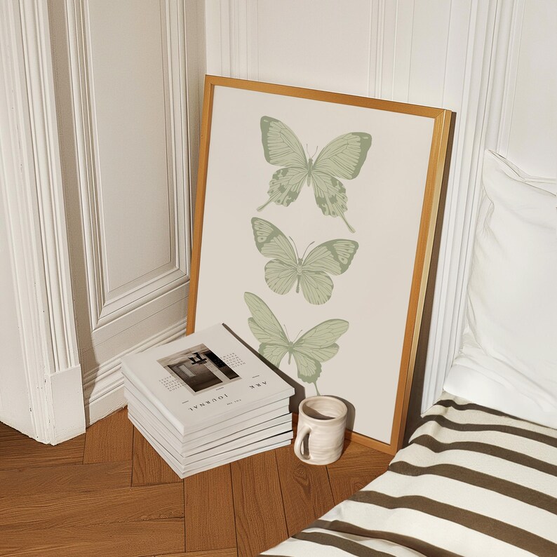 May include: A framed print with a pale green background featuring three stylised butterflies. The butterflies are arranged vertically, with the largest butterfly at the top and the smallest butterfly at the bottom. The frame is a light wood colour.
