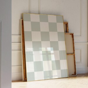 Puede incluir: Un lienzo grande enmarcado con un patr&oacute;n de tablero de ajedrez en tonos de blanco y verde claro. El lienzo est&aacute; apoyado contra una pared y est&aacute; rodeado de otros lienzos.