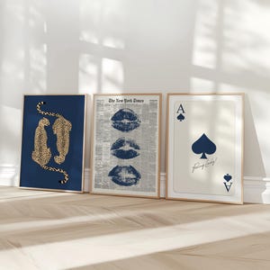 May include: Three framed art prints leaning against a wall. The prints feature a navy blue background with cheetahs, a newspaper print with blue lips, and an ace of spades playing card with the text "Feeling Lucky!"