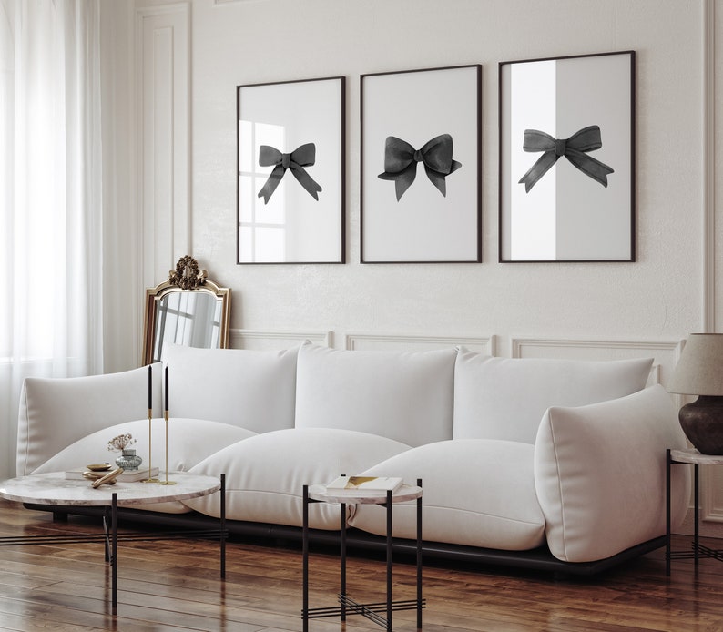 K&ouml;nnte beinhalten: Drei schwarz-wei&szlig;e gerahmte Drucke von schwarzen Aquarell-Schleifen auf wei&szlig;em Hintergrund. Die Drucke h&auml;ngen an einer wei&szlig;en Wand &uuml;ber einem wei&szlig;en Sofa.