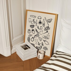 May include: A black and white illustration of various food items, including a baguette, croissant, grapes, lemons, shrimp, and a crab. The illustration is framed in a light wood frame and is hanging on a wall.