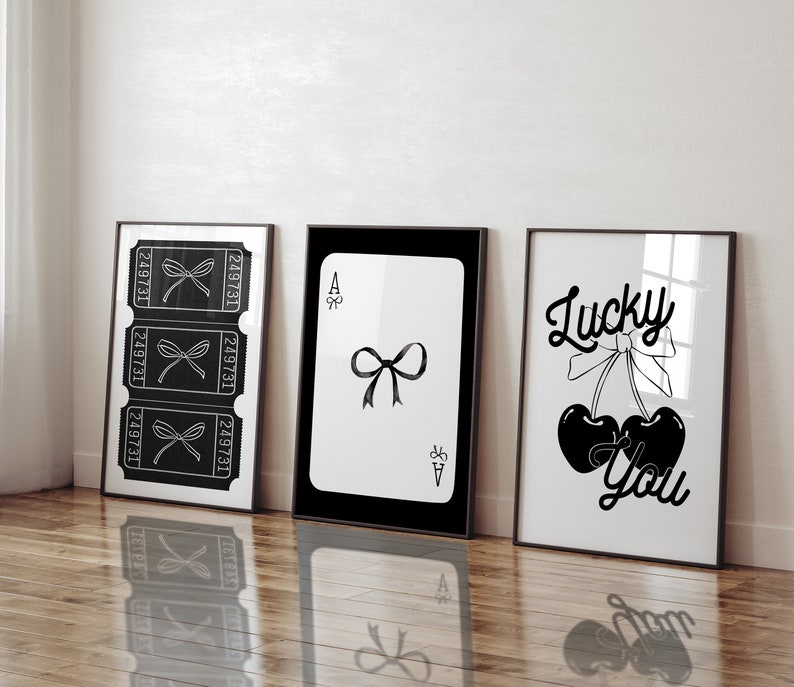 May include: Three black and white framed prints with different designs. The left print features three ticket stubs with a bow on each. The middle print features a playing card with a black bow on a white background. The right print features two cherries with a bow and the text "Lucky You".