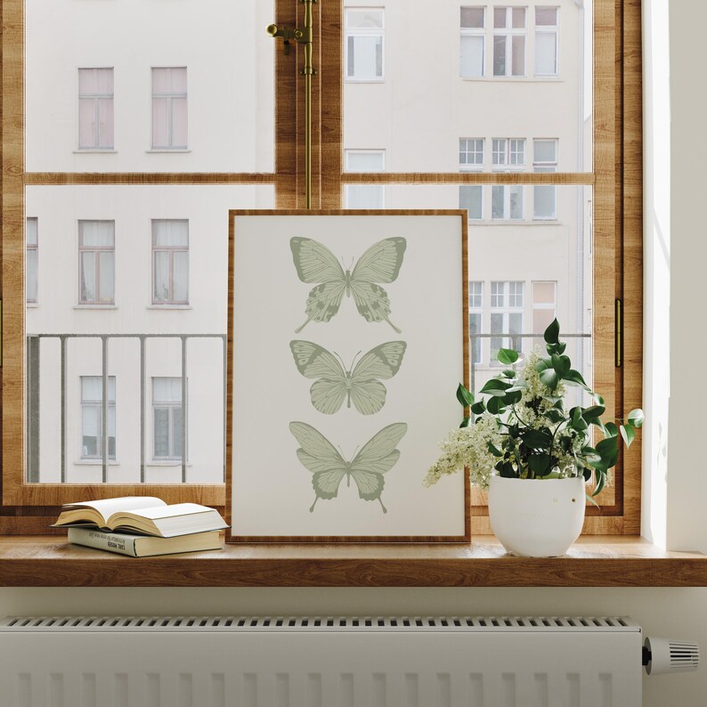 May include: A framed print with a minimalist design featuring three green butterflies in a vertical row on a white background.