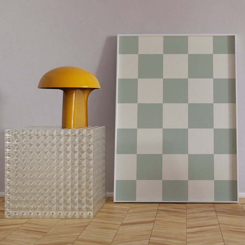 Puede incluir: Una l&aacute;mpara amarilla con forma de hongo se encuentra sobre una mesa de cubo de vidrio transparente frente a una impresi&oacute;n a cuadros verde y blanca enmarcada.